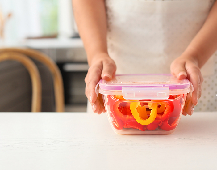 Photo of woman placing a lid on a container of red and yellow bell peppers